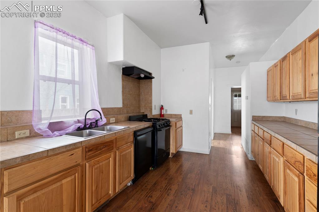 Kitchen featuring tile counters, dark wood finished floors, black appliances, and range hood