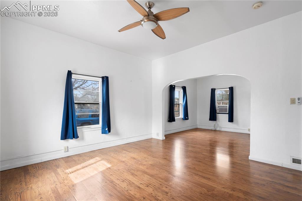 Empty room featuring a ceiling fan, wood finished floors, arched walkways, and plenty of natural light