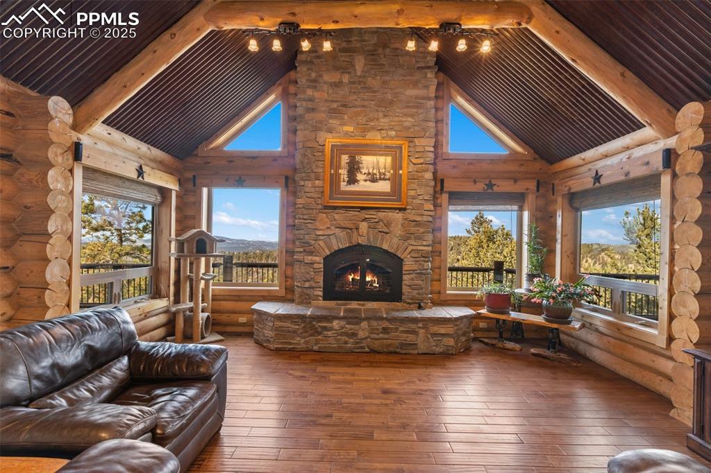 Living area featuring hardwood / wood-style floors, an outdoor stone fireplace, healthy amount of natural light, high vaulted ceiling, and log walls