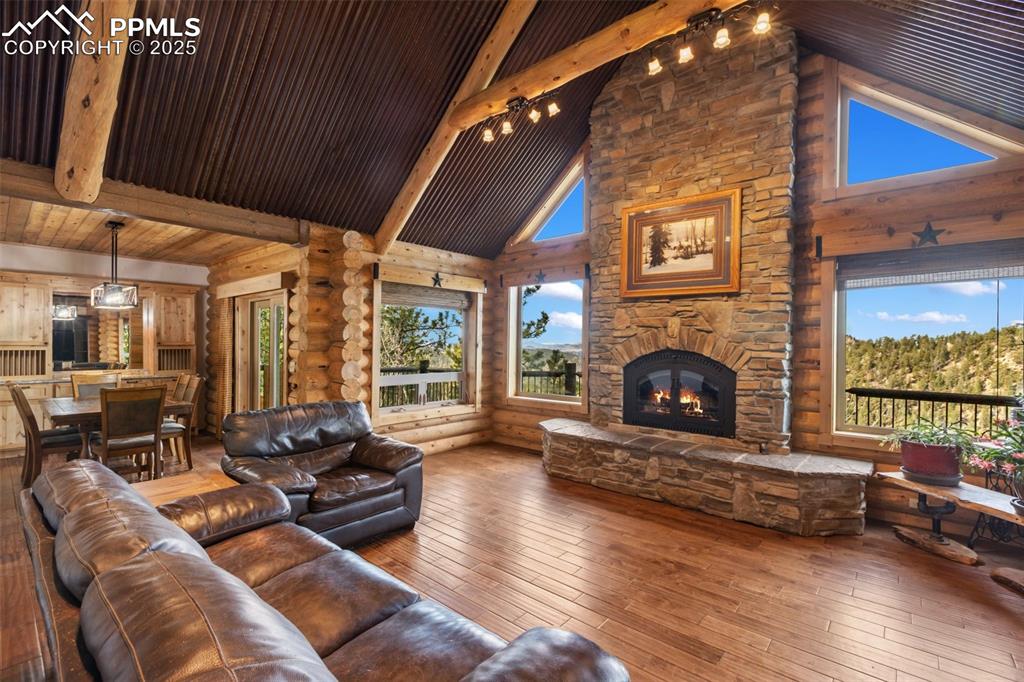 Living area featuring beamed ceiling, hardwood / wood-style flooring, high vaulted ceiling, plenty of natural light, and an outdoor stone fireplace