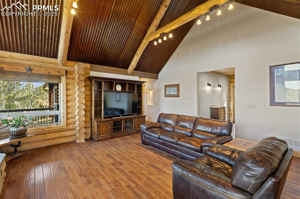 Living area featuring beamed ceiling, hardwood / wood-style floors, high vaulted ceiling, and rustic walls