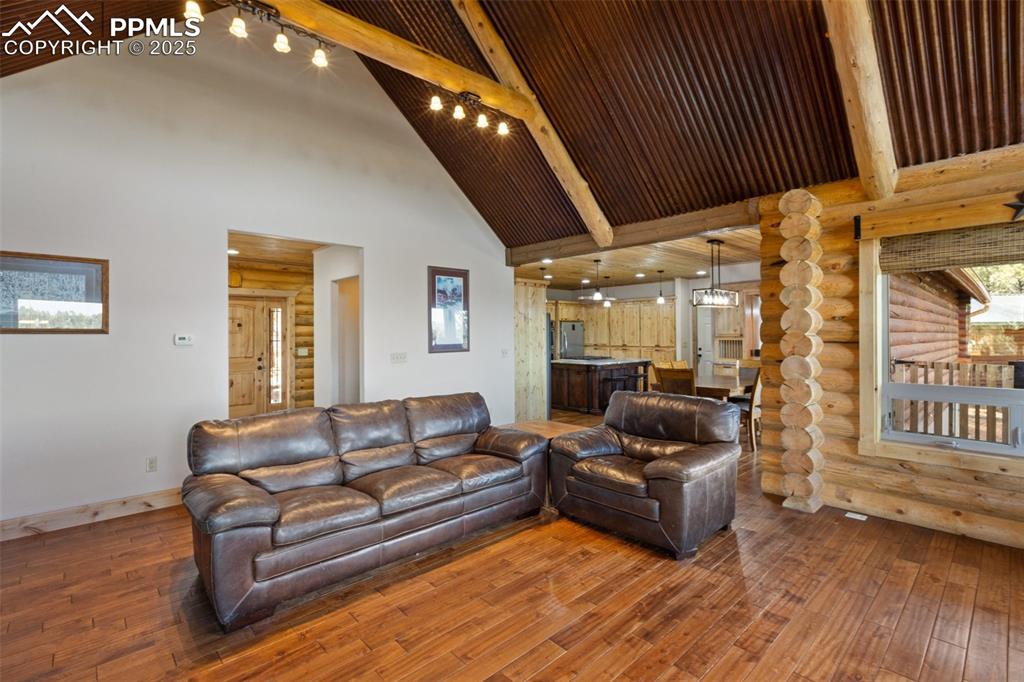 Living area featuring log walls, beamed ceiling, wood-type flooring, and high vaulted ceiling
