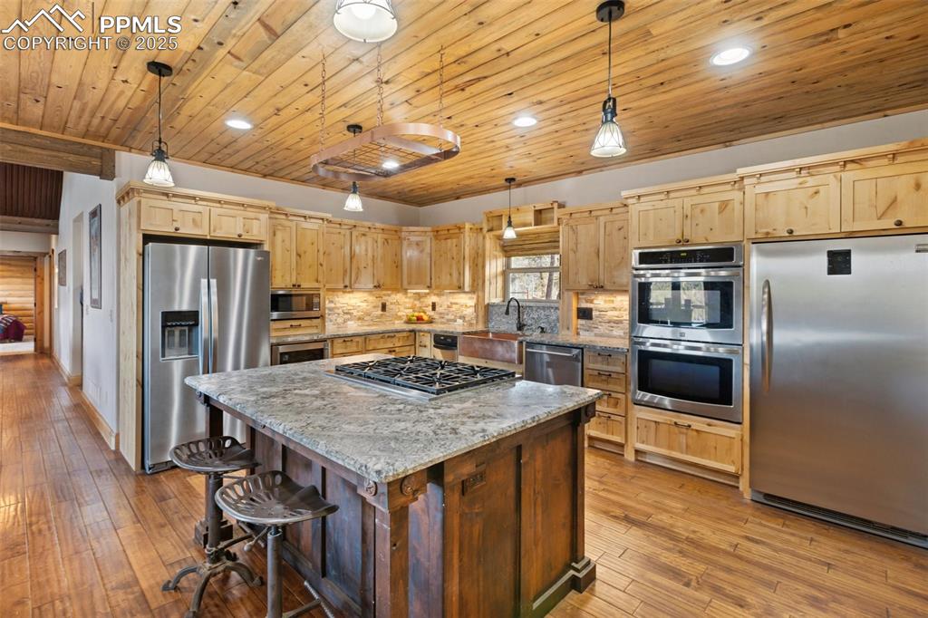 Kitchen with stainless steel appliances, light wood-type flooring, decorative backsplash, a center island, and light brown cabinets