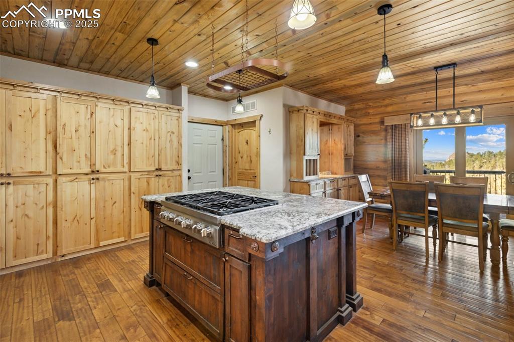 Kitchen with light stone counters, dark wood-type flooring, stainless steel gas stovetop, decorative light fixtures, and a center island