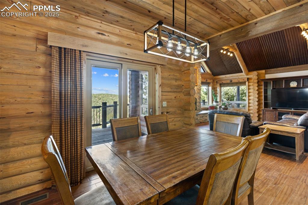 Dining space with rustic walls, a chandelier, a wooden ceiling with exposed beams, and hardwood / wood-style flooring