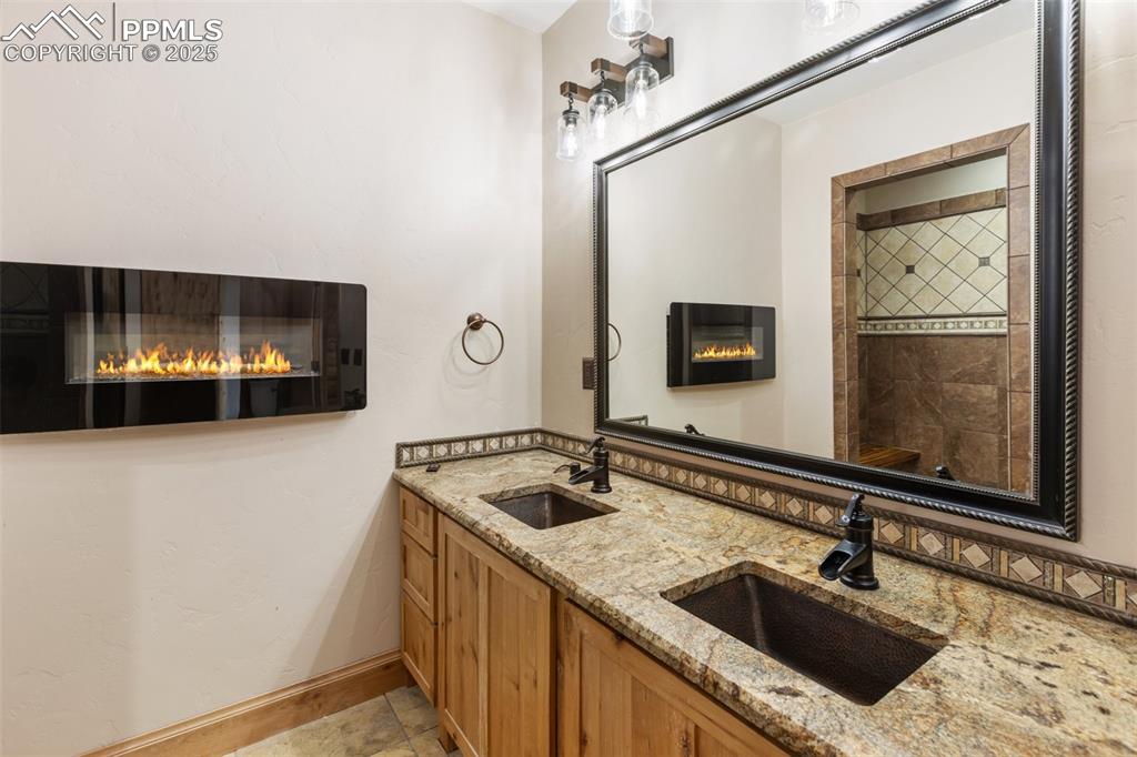 Bathroom with a glass covered fireplace, double vanity, and a tile shower
