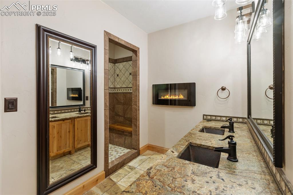 Full bathroom with double vanity, a stall shower, a glass covered fireplace, and light tile patterned flooring