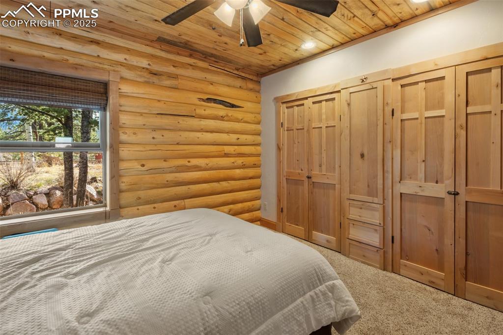 Bedroom with log walls, a closet, wood ceiling, carpet, and a ceiling fan