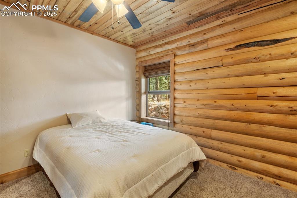 Bedroom featuring wood ceiling, rustic walls, carpet floors, and a ceiling fan