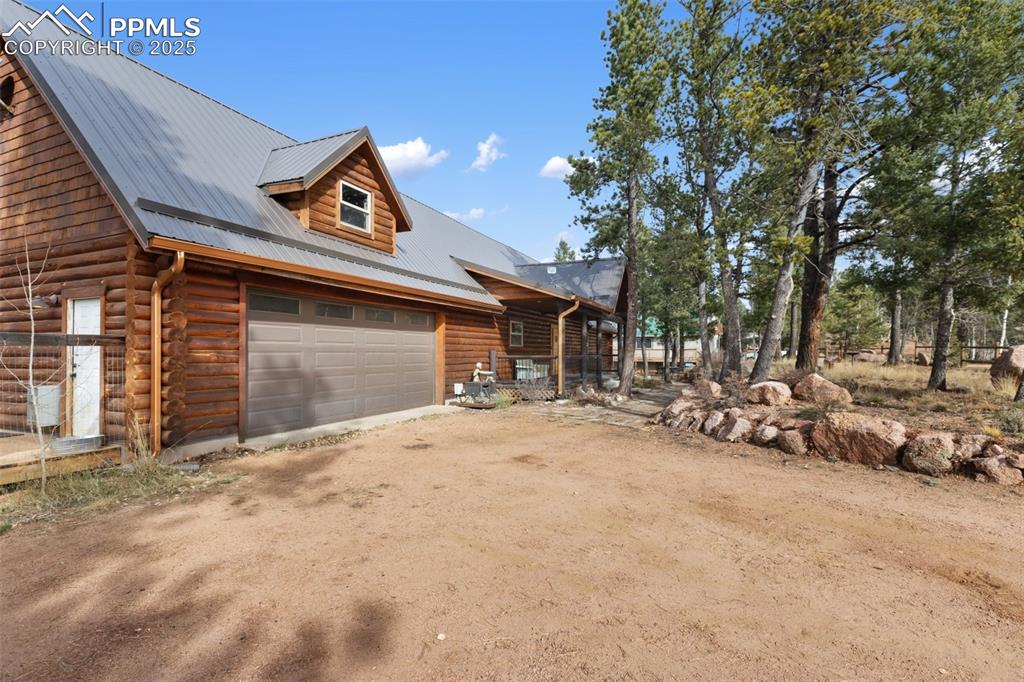 View of front of home featuring dirt driveway, log siding, a metal roof, and a garage