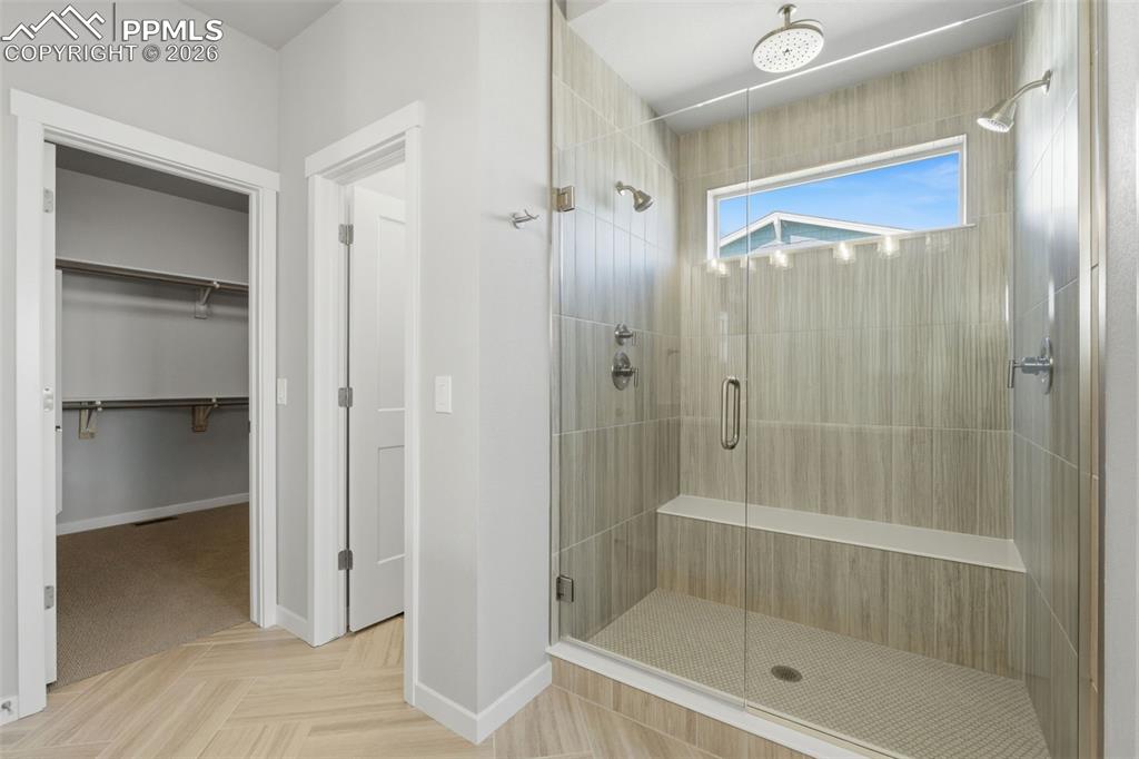 Stunning primary bathroom with floor-to-ceiling tile shower, frameless glass enclosure, and large windows