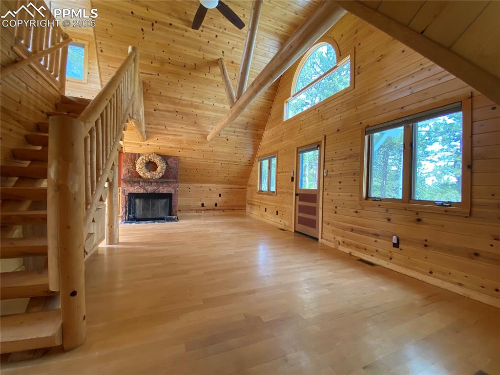 Living room featuring wooden walls, high vaulted ceiling with exposed beams, and a wood burning fireplace
