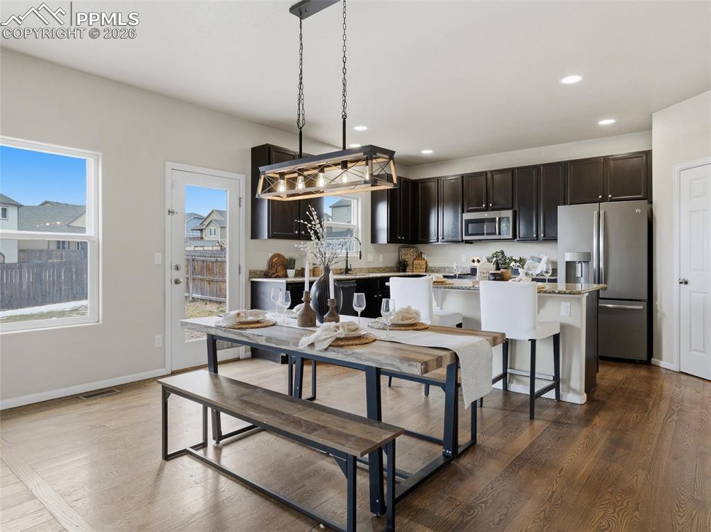 Kitchen with appliances with stainless steel finishes, a center island, light stone countertops, dark wood-type flooring, and a breakfast bar area