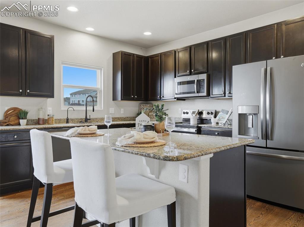Kitchen featuring appliances with stainless steel finishes, a kitchen island, light stone countertops, dark wood-style flooring, and a kitchen bar