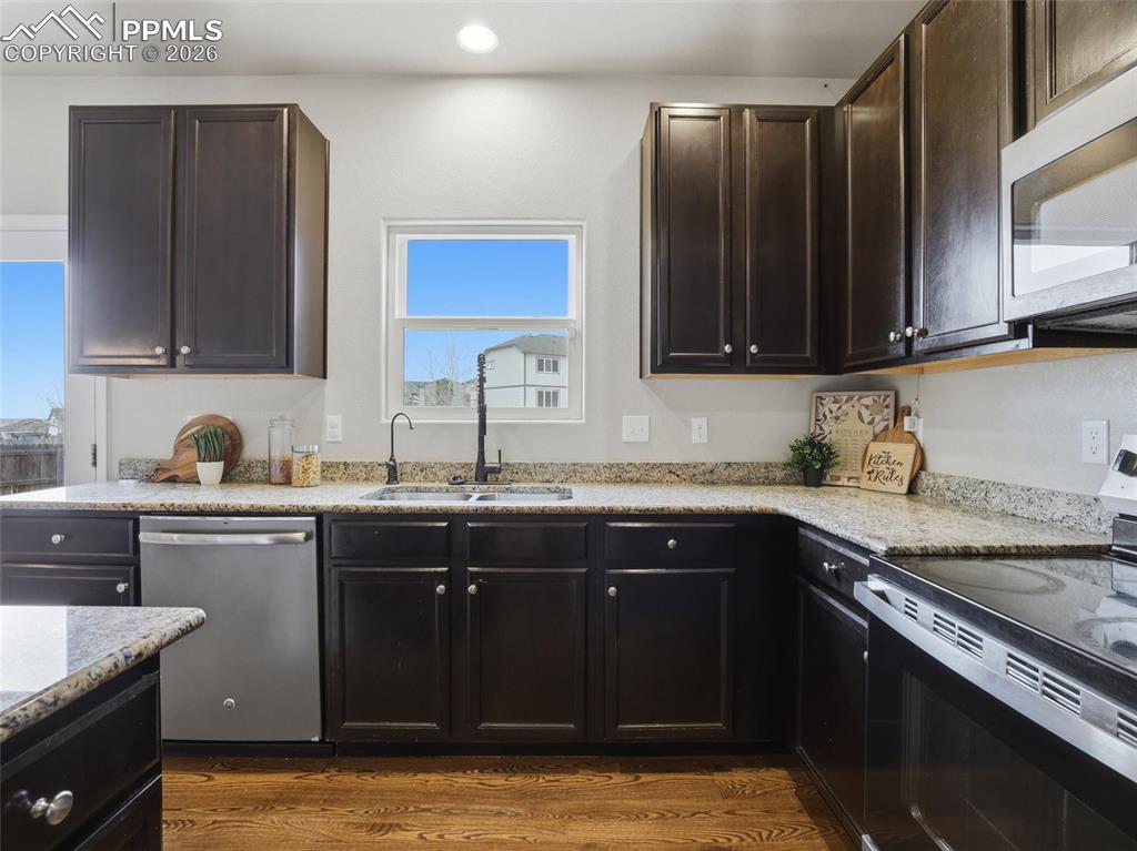 Kitchen featuring stainless steel appliances, light stone counters, dark wood-style flooring, dark brown cabinetry, and recessed lighting