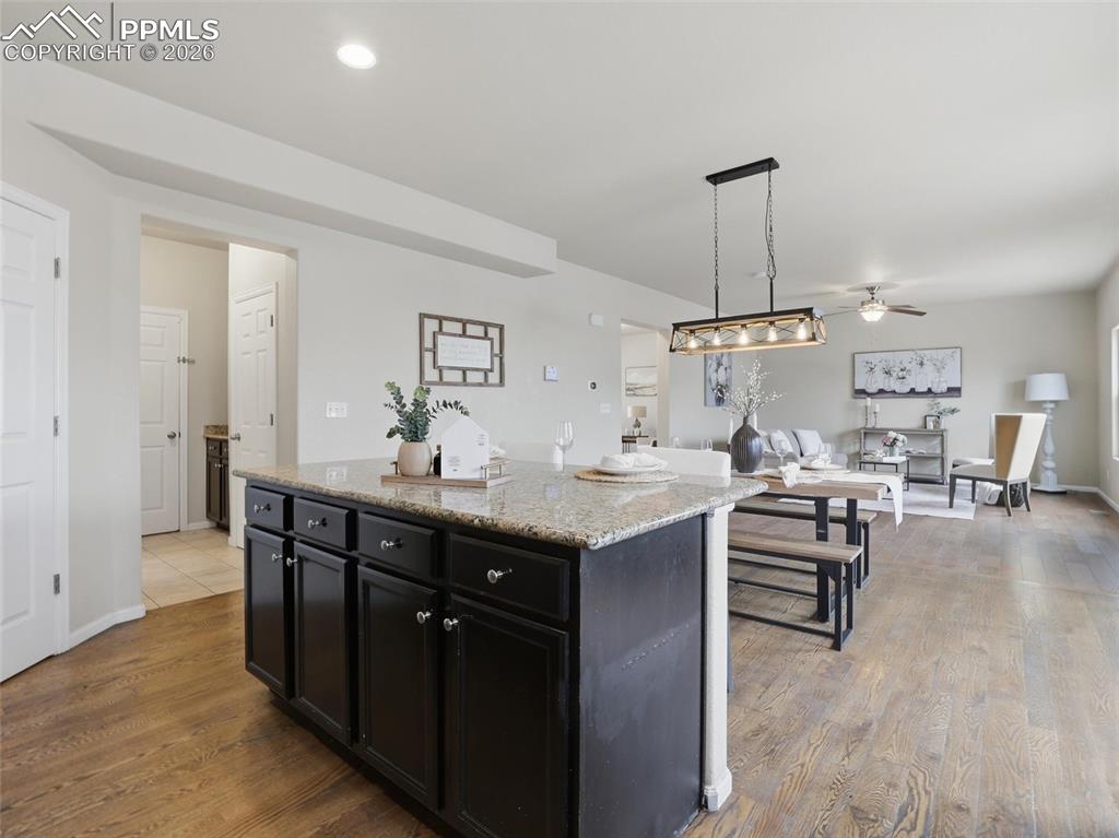 Kitchen with dark cabinetry, decorative light fixtures, light stone countertops, a ceiling fan, and a center island