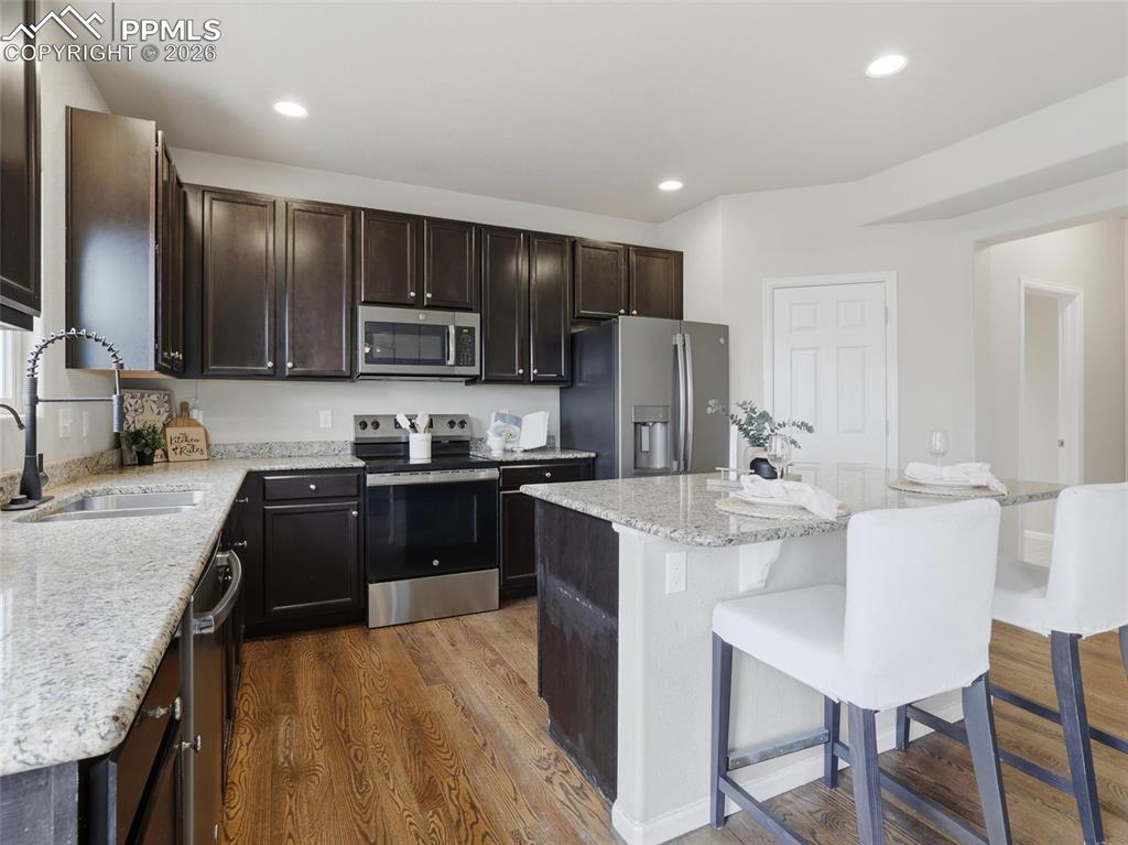 Kitchen featuring stainless steel appliances, light stone counters, dark wood finished floors, a kitchen island, and a kitchen bar