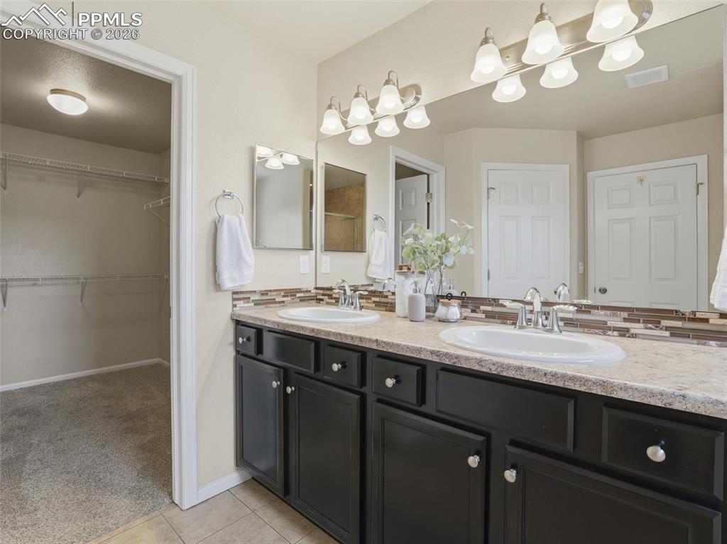 Bathroom with double vanity, a spacious closet, light colored carpet, and light tile patterned floors