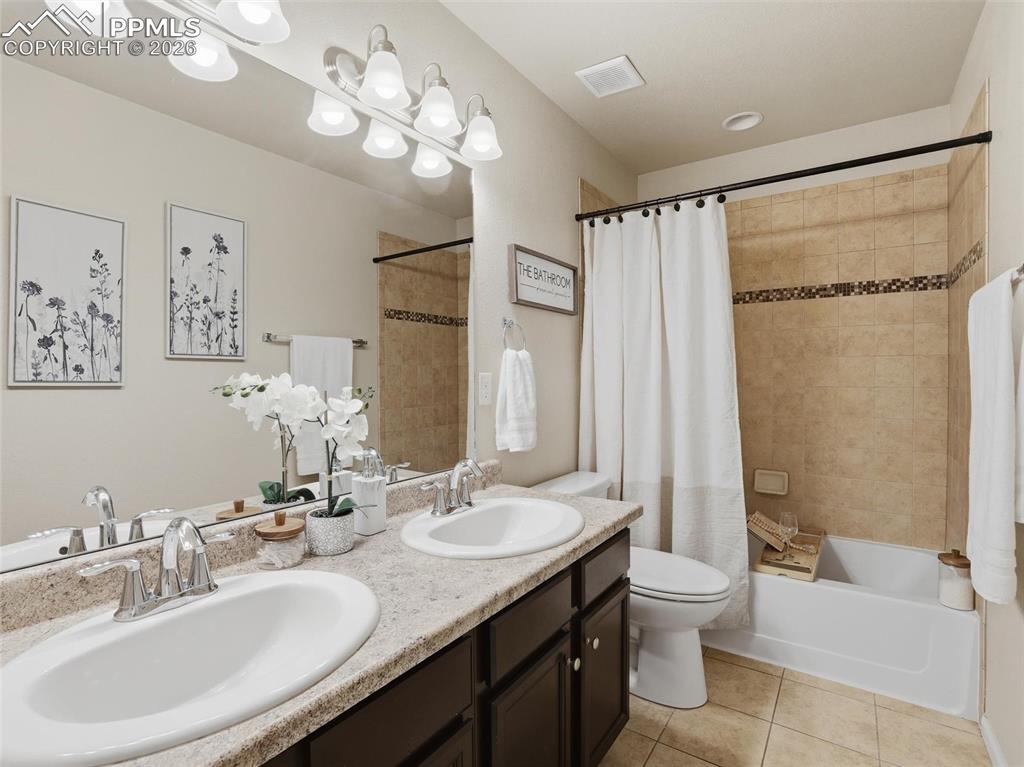 Full bathroom featuring double vanity, shower / bath combination with curtain, and light tile patterned flooring