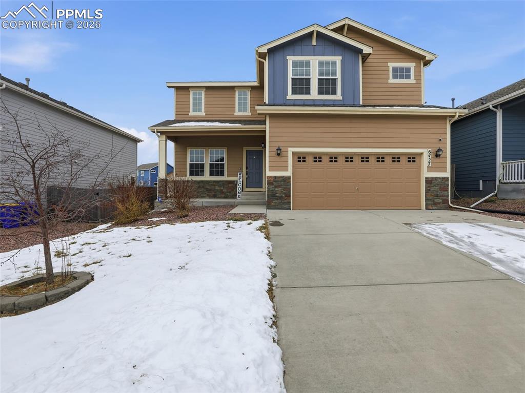 View of front of property with stone siding, covered porch, board and batten siding, and an attached garage