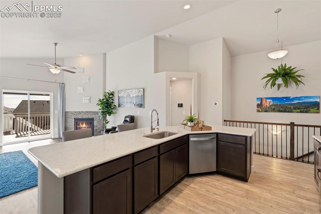 Kitchen featuring lofted ceiling, dark wood finish cabinetry, a fireplace, decorative light fixtures, and dishwasher