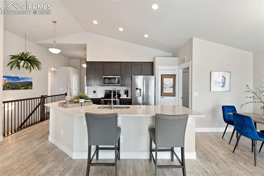 Kitchen with stainless steel appliances, vaulted ceiling, dark wood finish cabinetry, an island with sink, and pendant lighting