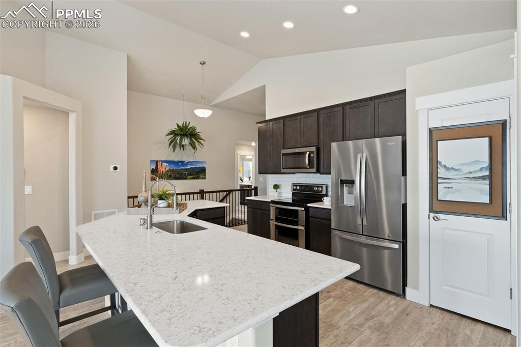 Kitchen with stainless steel appliances, dark wood finish cabinets, a breakfast bar, light wood-type flooring, and a center island with sink
