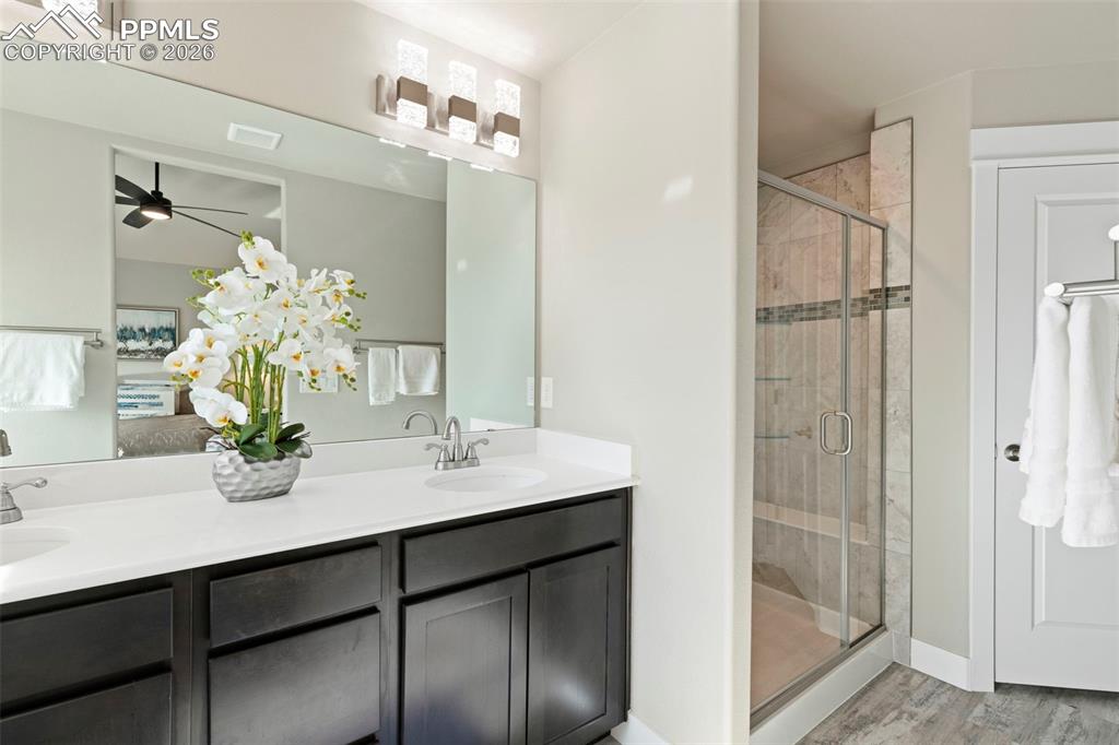 Full bath featuring double vanity, a stall shower, ceiling fan, and light wood-style floors