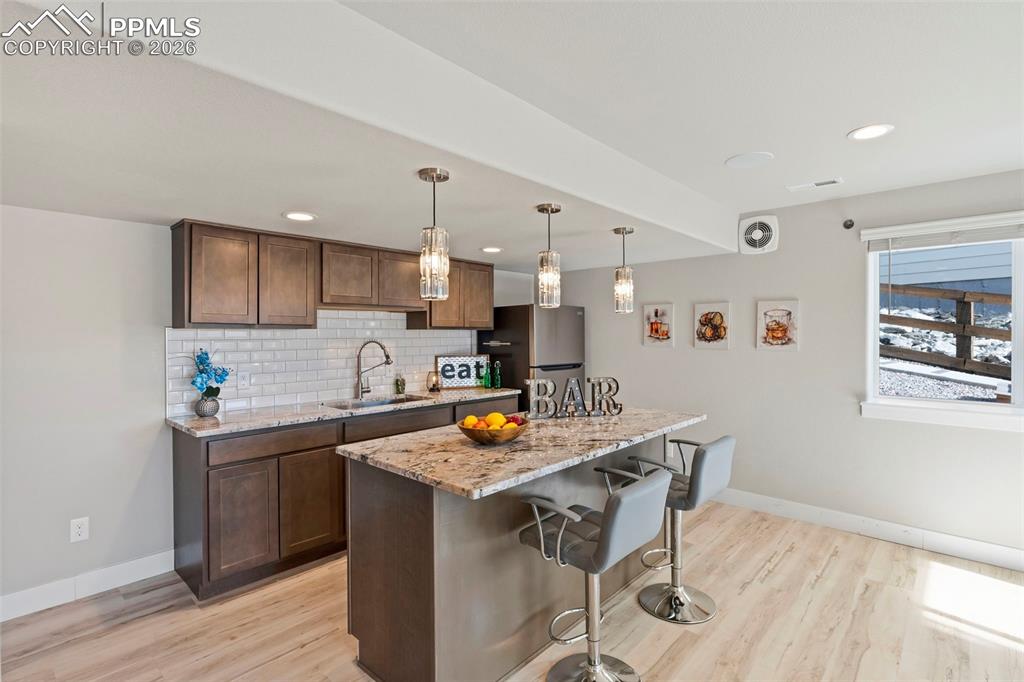 2nd Kitchenette/wet bar with a kitchen bar, a center island, decorative light fixtures, light stone counters, and light wood finished floors