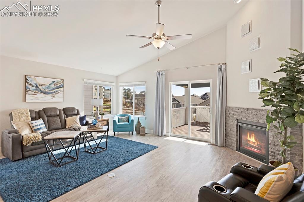 Living area with lofted ceiling, ceiling fan, a glass covered fireplace, and wood finished floors