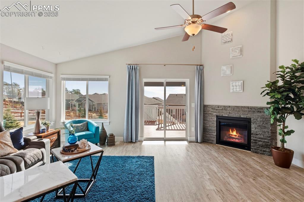 Living area featuring vaulted ceiling, light wood-style floors, a fireplace, and a ceiling fan