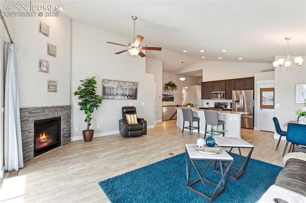 Living area with light wood-style flooring, a ceiling fan, a fireplace, vaulted ceiling, and a chandelier