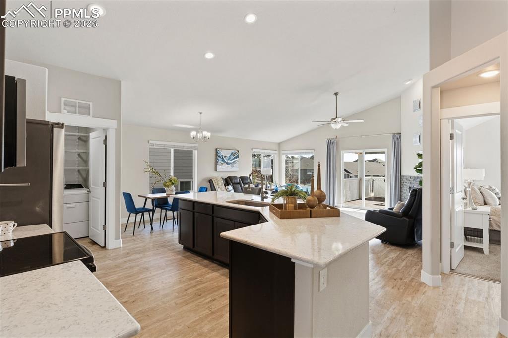 Kitchen with open floor plan, freestanding refrigerator, light wood-style floors, vaulted ceiling, and hanging lights