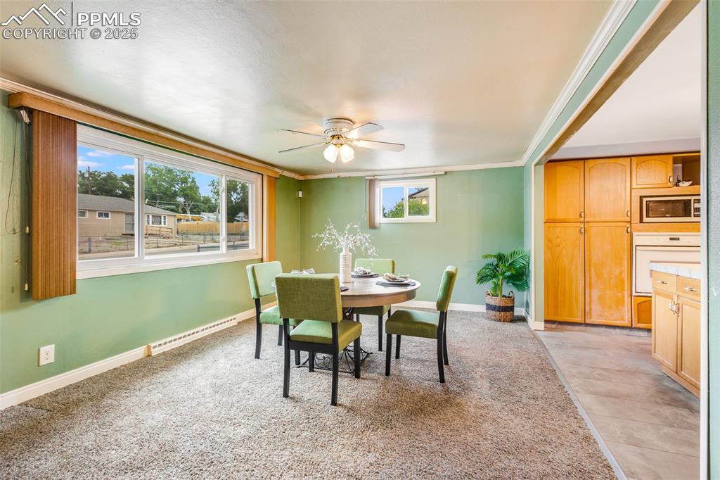 Dining area featuring ornamental molding, baseboard heating, a ceiling fan, and light carpet