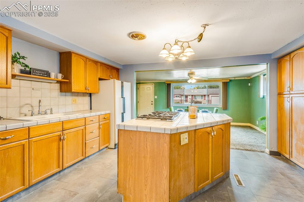 Kitchen featuring backsplash, freestanding refrigerator, tile counters, open shelves, and stainless steel gas stovetop