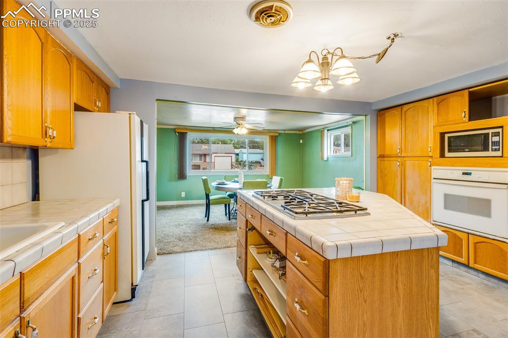 Kitchen with appliances with stainless steel finishes, tile counters, open shelves, a center island, and a ceiling fan