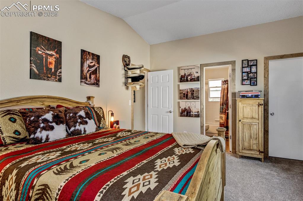 Bedroom featuring light colored carpet, vaulted ceiling, and ensuite bath