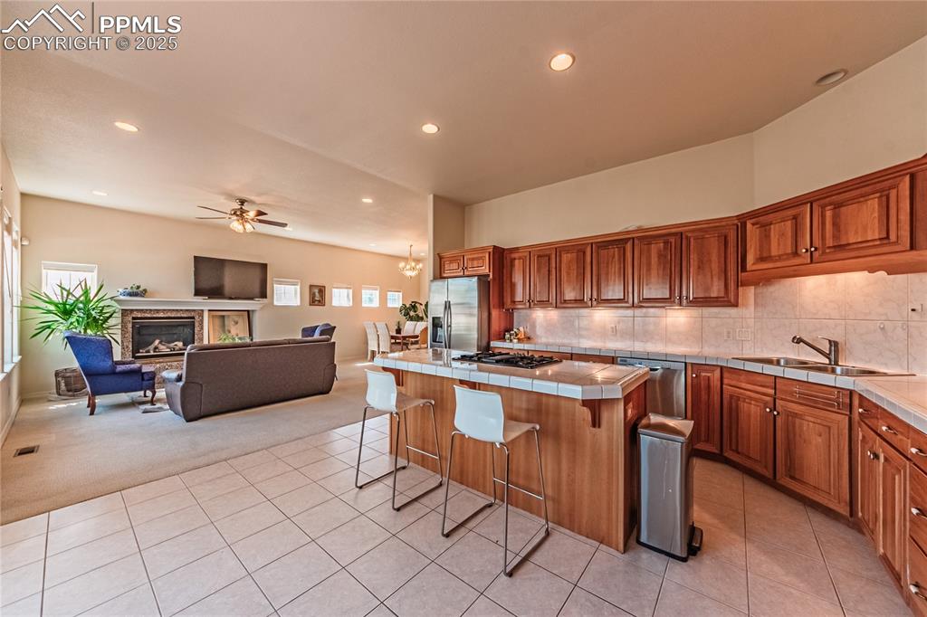 Kitchen with tile counters, light carpet, light tile patterned floors, appliances with stainless steel finishes, and a sink