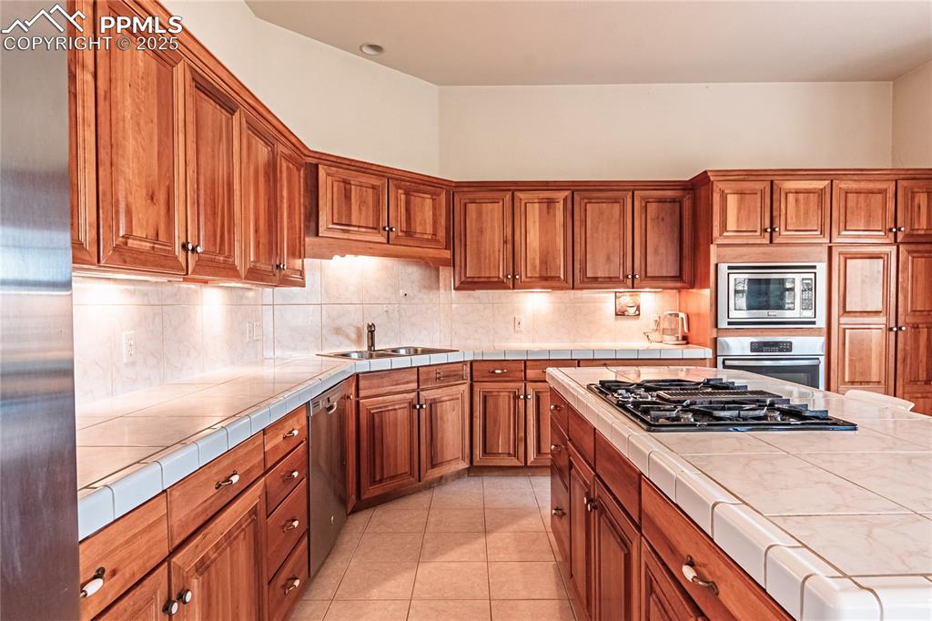 Kitchen with brown cabinets, a sink, appliances with stainless steel finishes, and tile counters