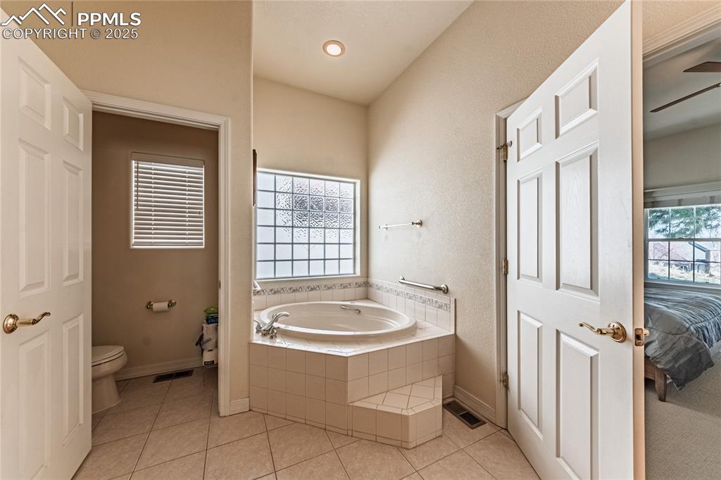 Ensuite bathroom featuring toilet, a bath, tile patterned flooring, and visible vents