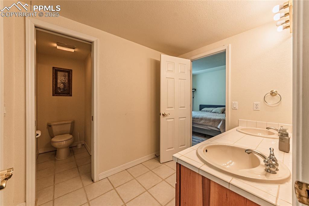Ensuite bathroom with a textured ceiling, toilet, a sink, tile patterned floors, and double vanity