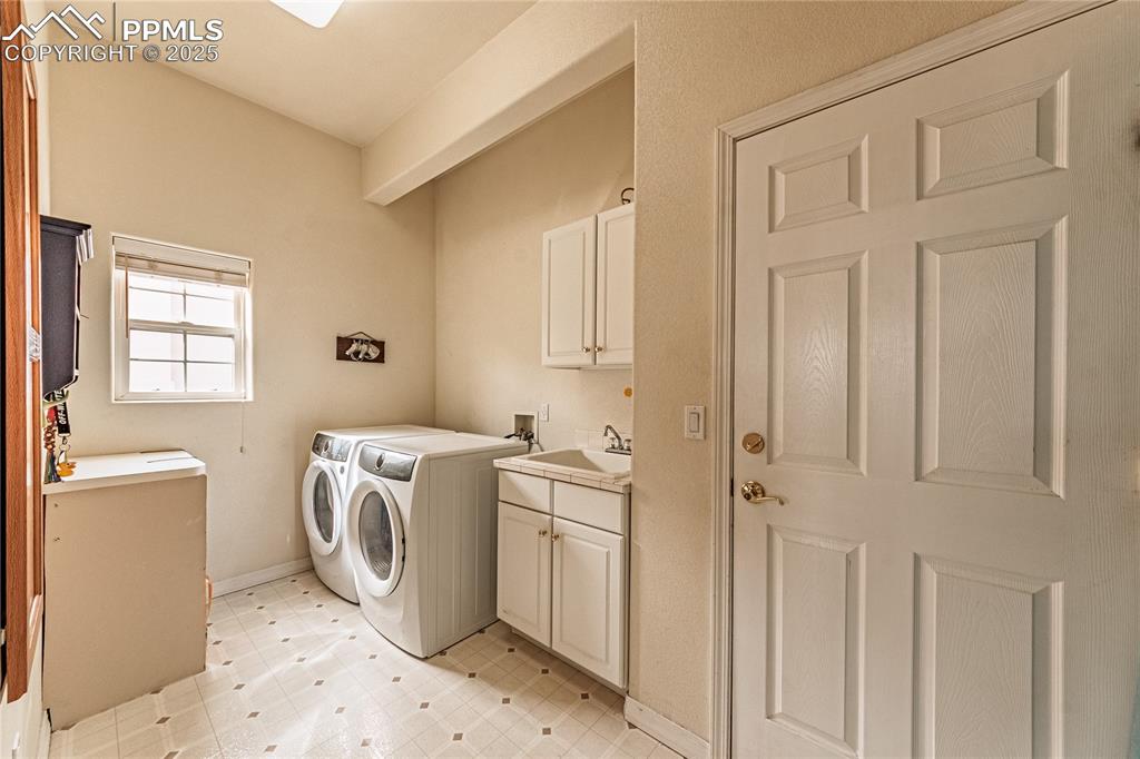 Washroom with light floors, washing machine and clothes dryer, a sink, baseboards, and cabinet space
