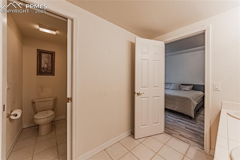 Ensuite bathroom with ensuite bathroom, a textured ceiling, tile patterned flooring, toilet, and baseboards