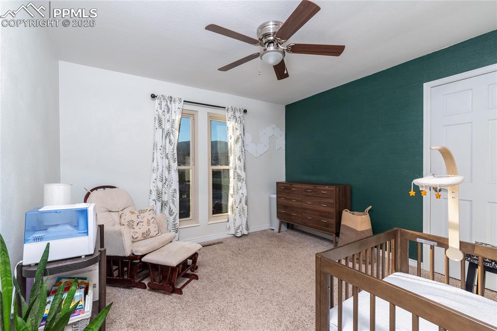 Carpeted bedroom with a crib and ceiling fan