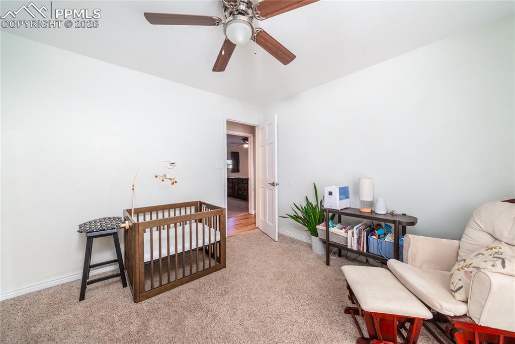 Carpeted bedroom with a crib and a ceiling fan