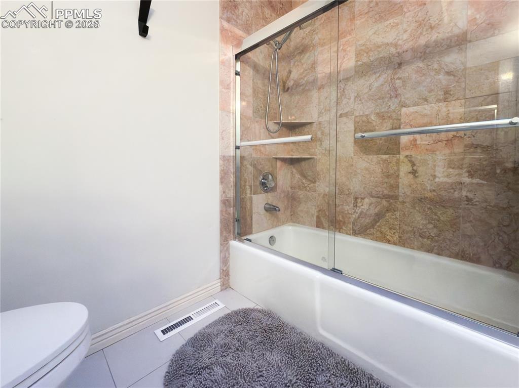Full bath featuring bath / shower combo with glass door and tile patterned flooring