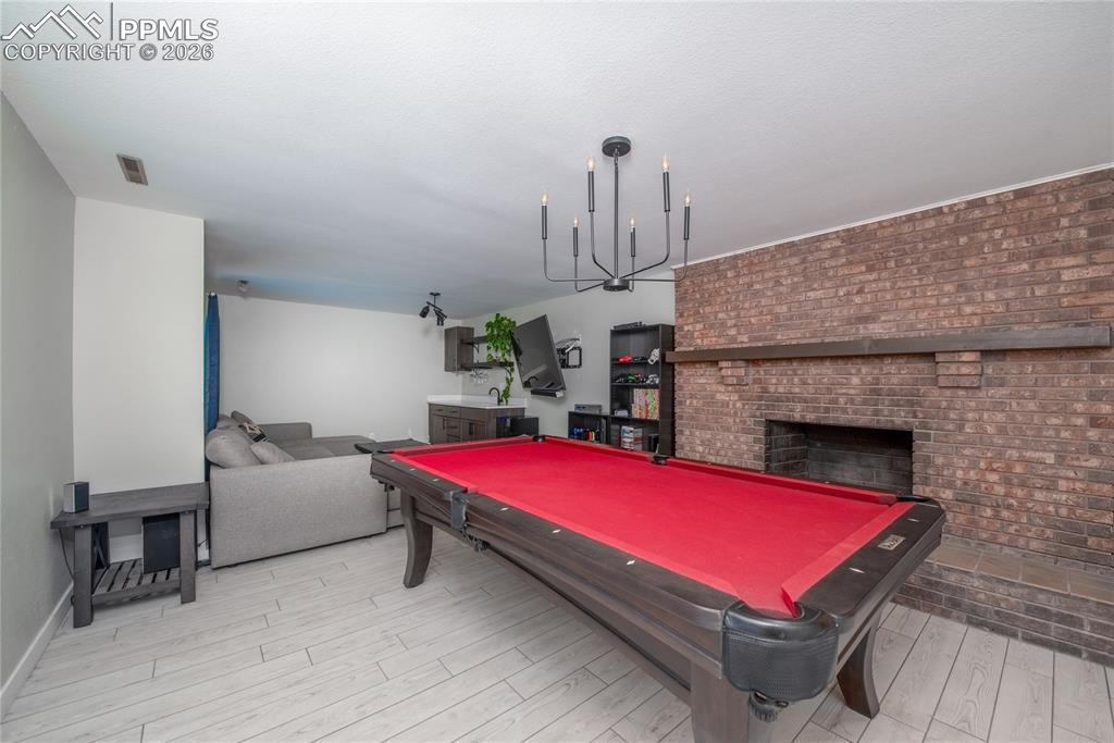 Rec room featuring pool table, a brick fireplace, light wood-type flooring, and brick wall