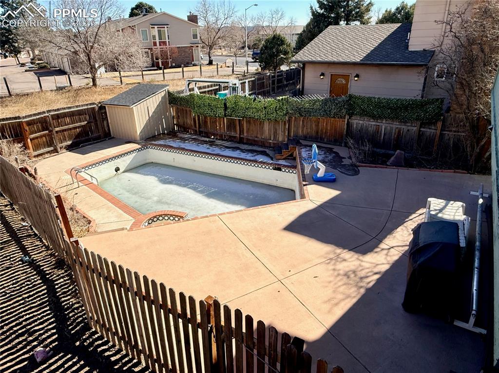 View of pool with a fenced backyard, a storage shed, an empty pool, and patio surround