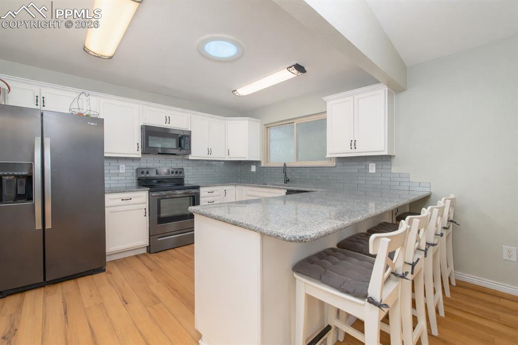 Kitchen featuring stainless steel appliances, a breakfast bar, light stone counters, a peninsula, and light wood-type flooring