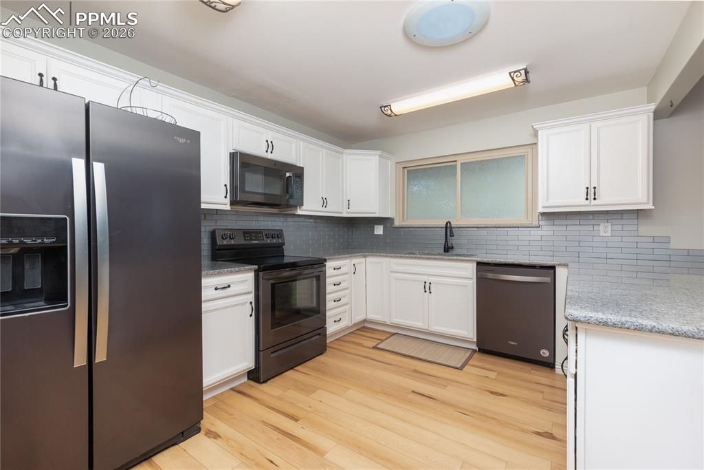 Kitchen with stainless steel appliances, white cabinets, light wood-style flooring, and light stone countertops